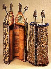 An open torah scroll on rollers in an ornate case and a closed case in a similar style